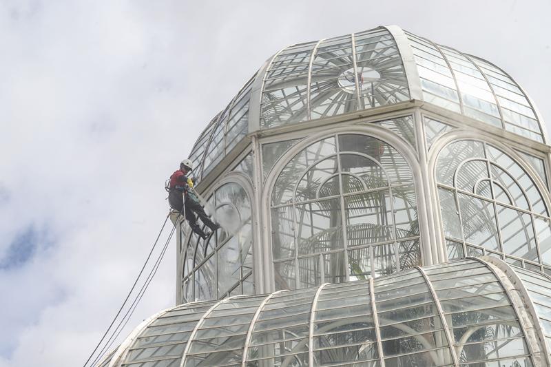 Com equipamentos de rapel, funcionário faz limpeza dos vidros da cúpula da estufa do Jardim Botânico
